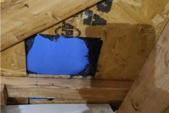 An opening in wooden structure covered with black tape and a blue sheet.