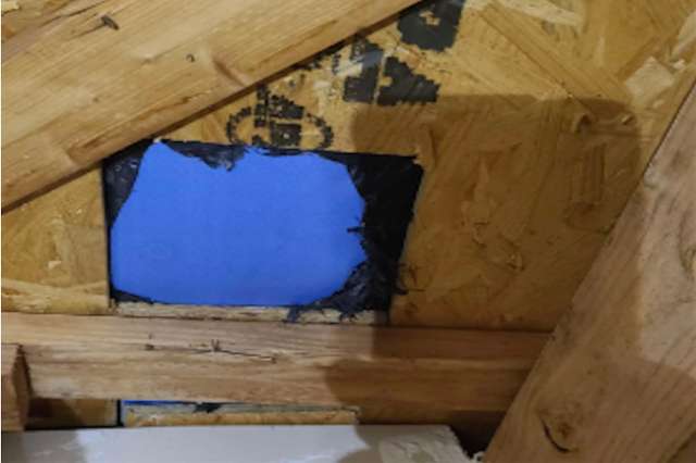 An opening in wooden structure covered with black tape and a blue sheet.