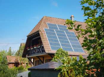 A house with solar panels on the roof surrounded by greenery.