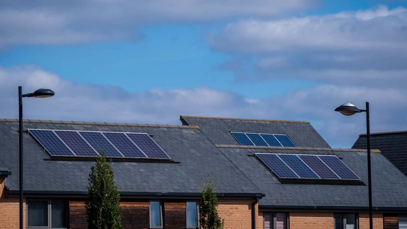 Solar panels installed on the roofs of residential buildings under a partly cloudy sky.