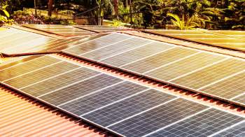 Solar panels installed on a red metal roof surrounded by greenery.