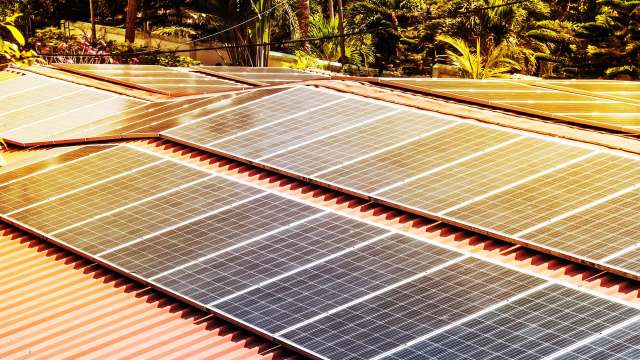 Solar panels installed on a red metal roof surrounded by greenery.