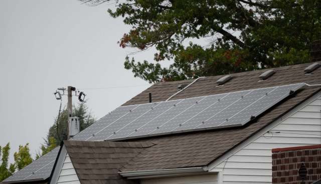 A house roof with solar panels and a power pole in the background.