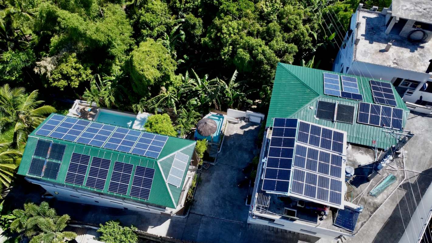 Two buildings with green roofs covered in solar panels, surrounded by dense greenery and a pool area.