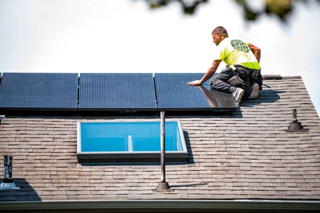A worker installs solar panels on a sloped roof.