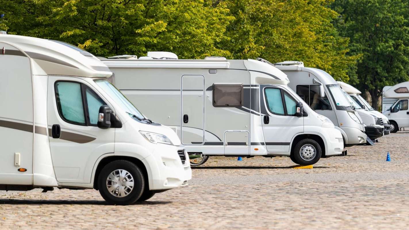 Several recreational vehicles parked in a lined row on a cobblestone surface surrounded by greenery.