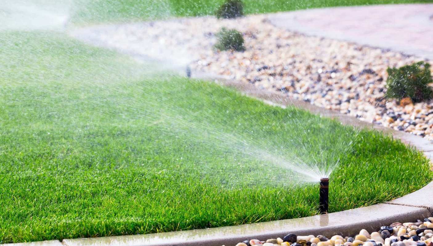 A lawn sprinkler sprays water onto green grass near a stone path.