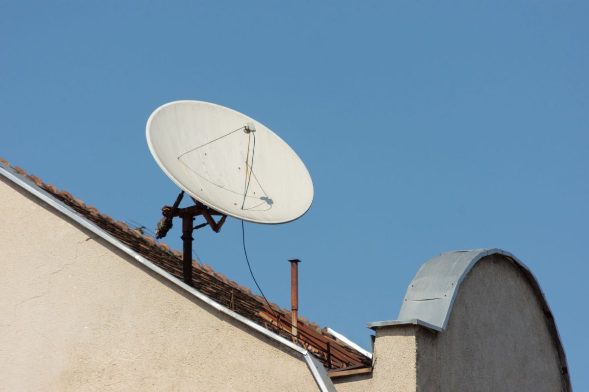 A satellite dish installed on the roof of a building against a clear blue sky.