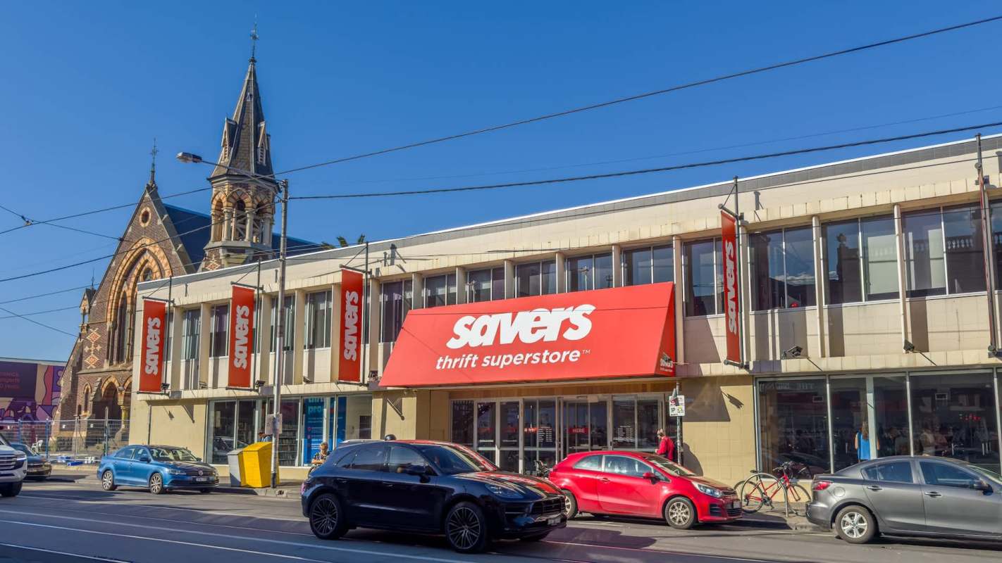 A Savers thrift store building with a large red sign and parked cars in front.