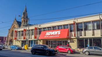 A Savers thrift store building with a large red sign and parked cars in front.