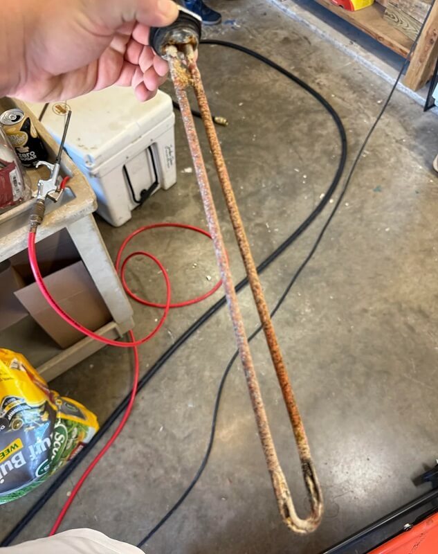 A close-up of a corroded heating element attached to a black circular base, positioned near metallic fittings.