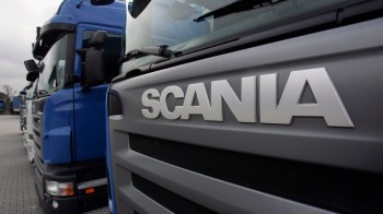 A row of Scania trucks parked with a focus on the Scania logo on the front of one truck.