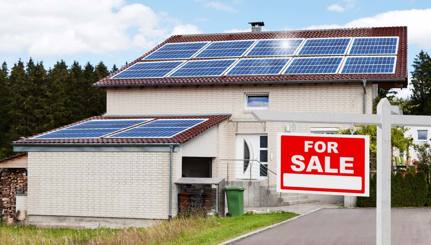 A house with solar panels and a "For Sale" sign in front.