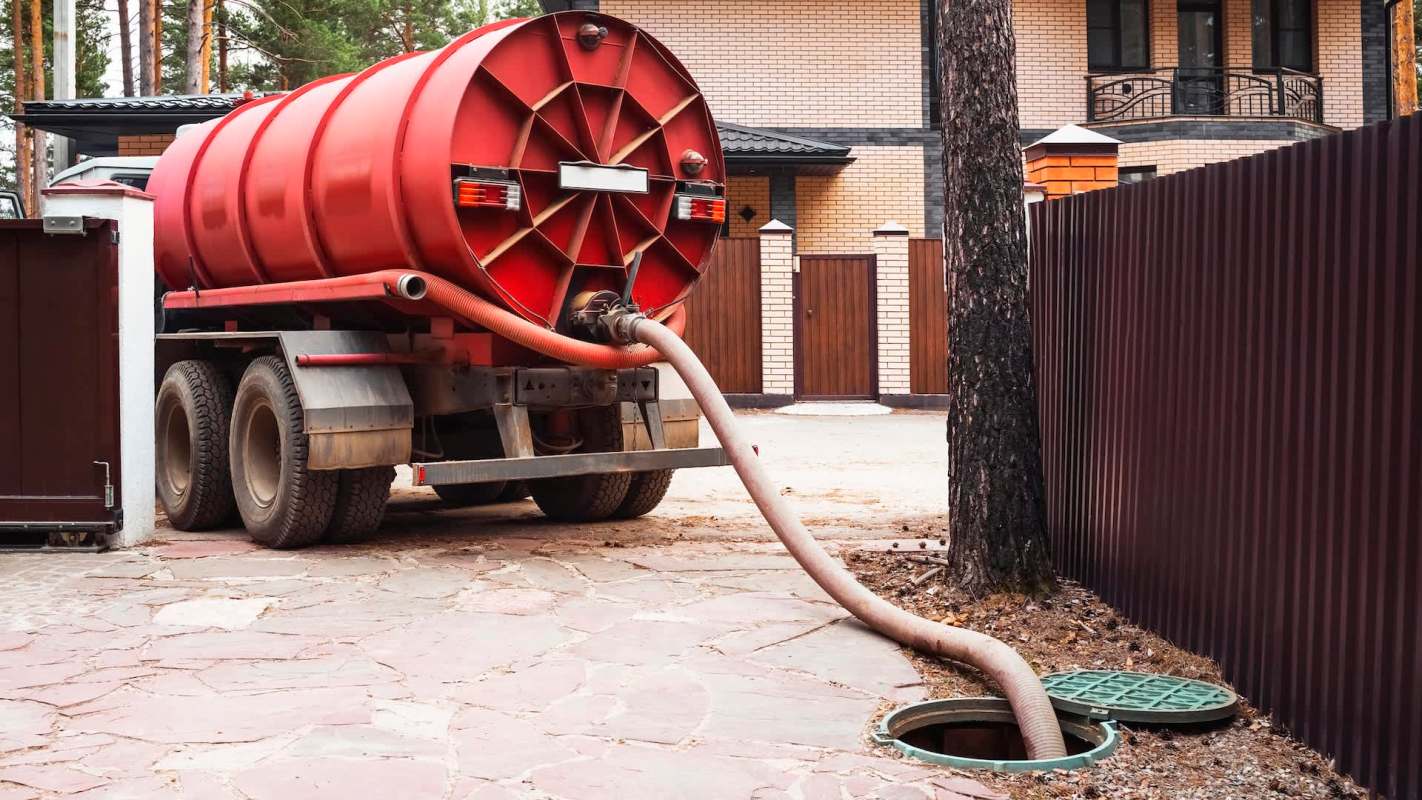 A red sewage truck with a hose attached is positioned near a manhole in a residential area.