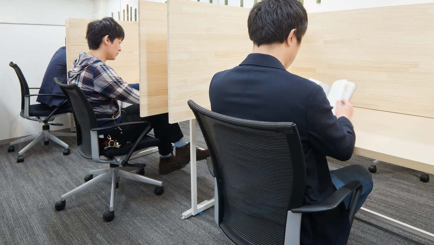 Two individuals seated at workstations in a modern indoor setting, focused on their tasks.