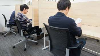Two individuals seated at workstations in a modern indoor setting, focused on their tasks.