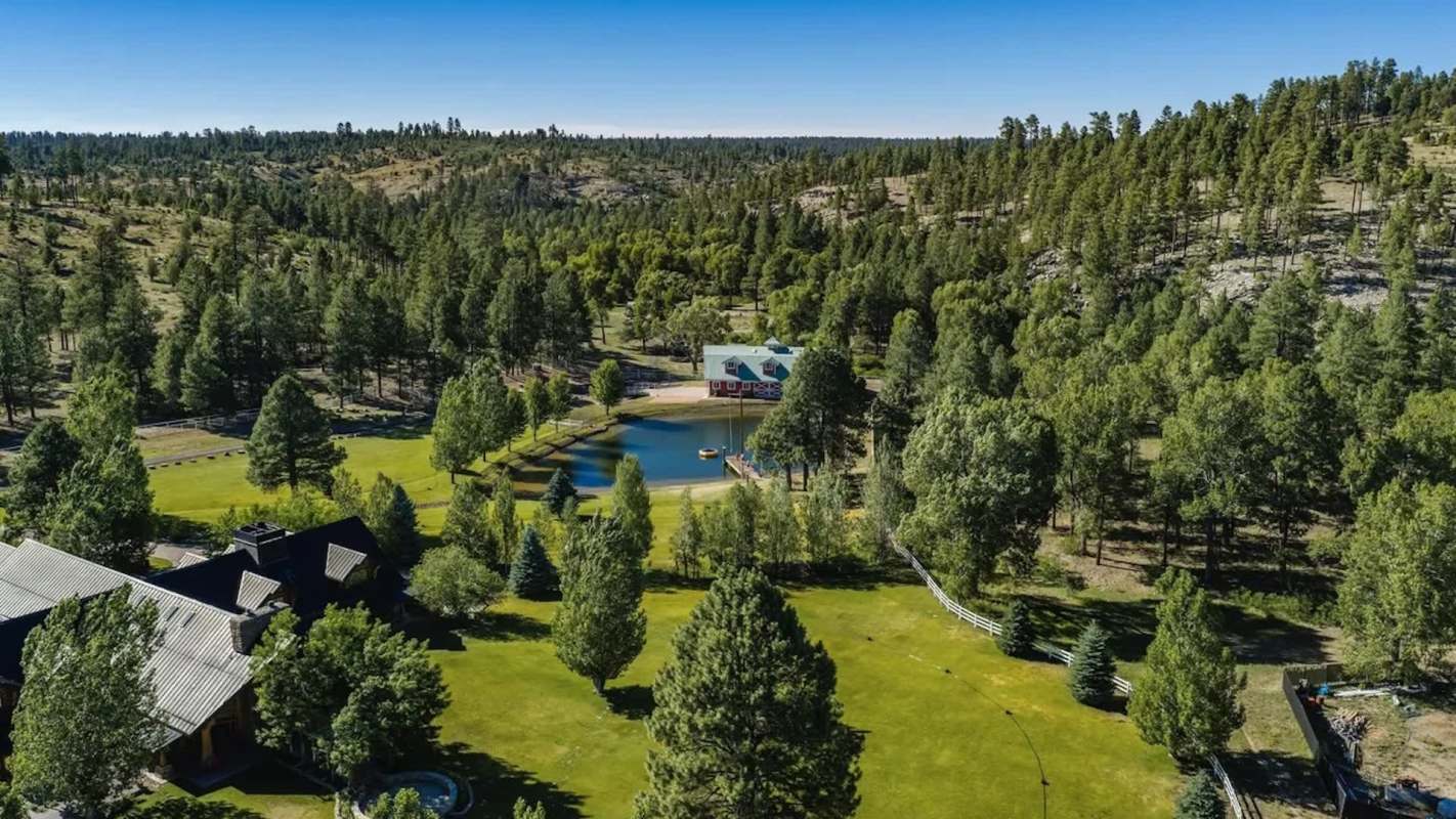A green landscape featuring a pond, surrounded by trees and a building with a blue roof.