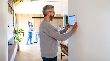 A man adjusts a thermostat on the wall in a modern living space.