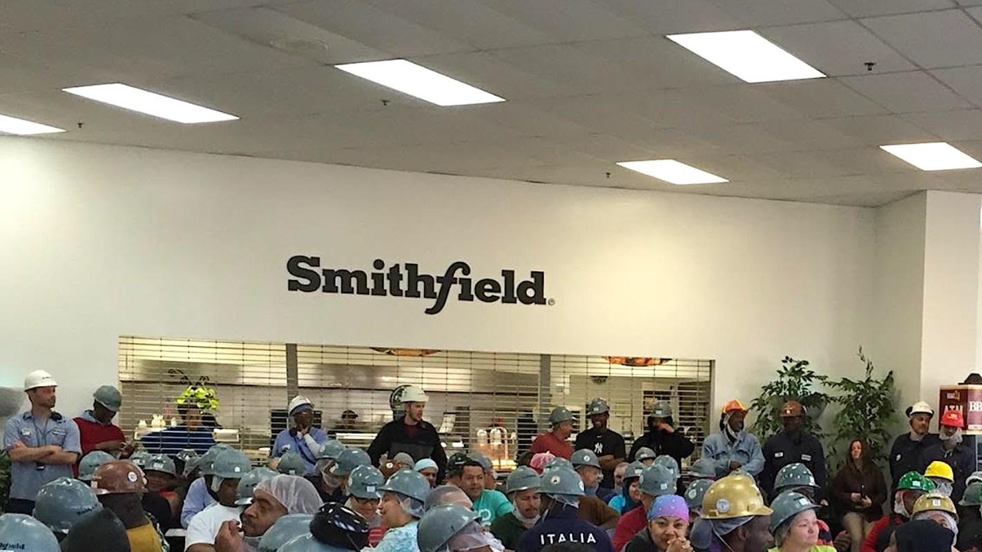 A group of people wearing helmets and hairnets in a Smithfield facility.