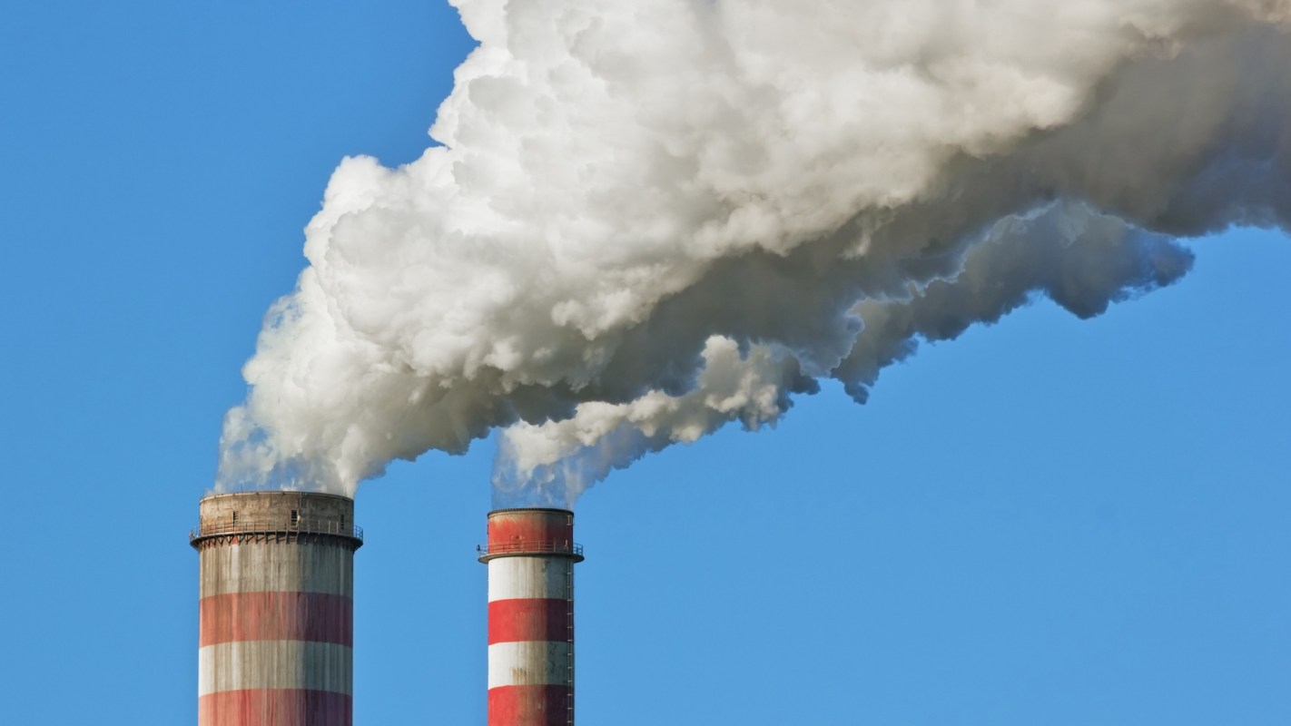Two industrial smokestacks emitting large plumes of white smoke against a clear blue sky.