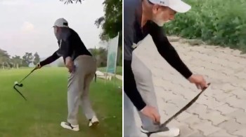 A person swings a golf club on a grassy area and gets ready to release a snake on a paved surface.