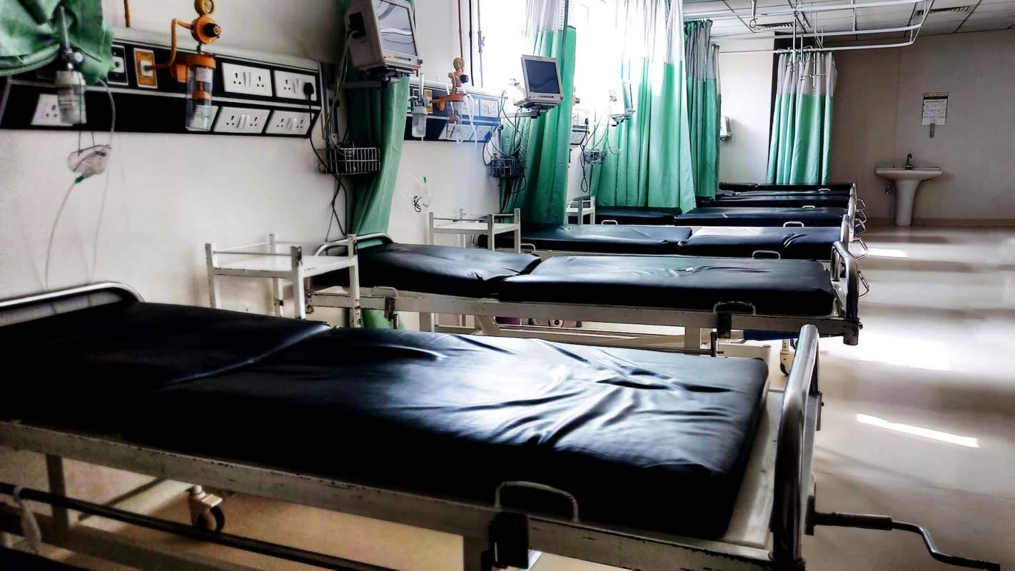 A hospital room with several empty hospital beds and green privacy curtains.