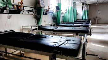 A hospital room with several empty hospital beds and green privacy curtains.