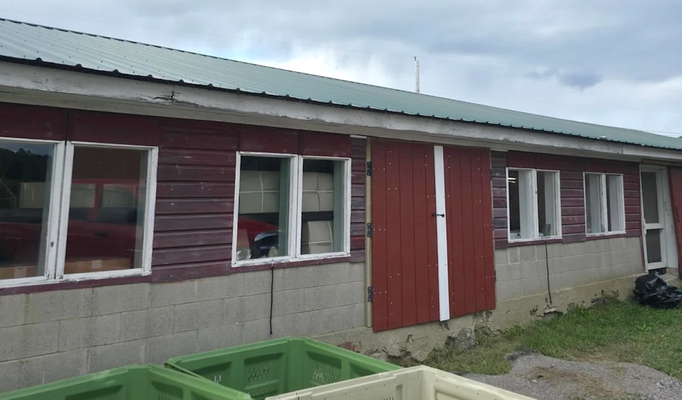 A building with a red and gray exterior, featuring several windows and green storage bins in front.