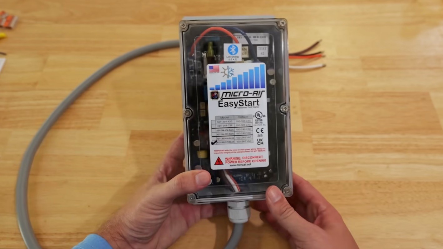 A person holding a Micro-Air EasyStart soft start device with electrical wires and a gray cord.