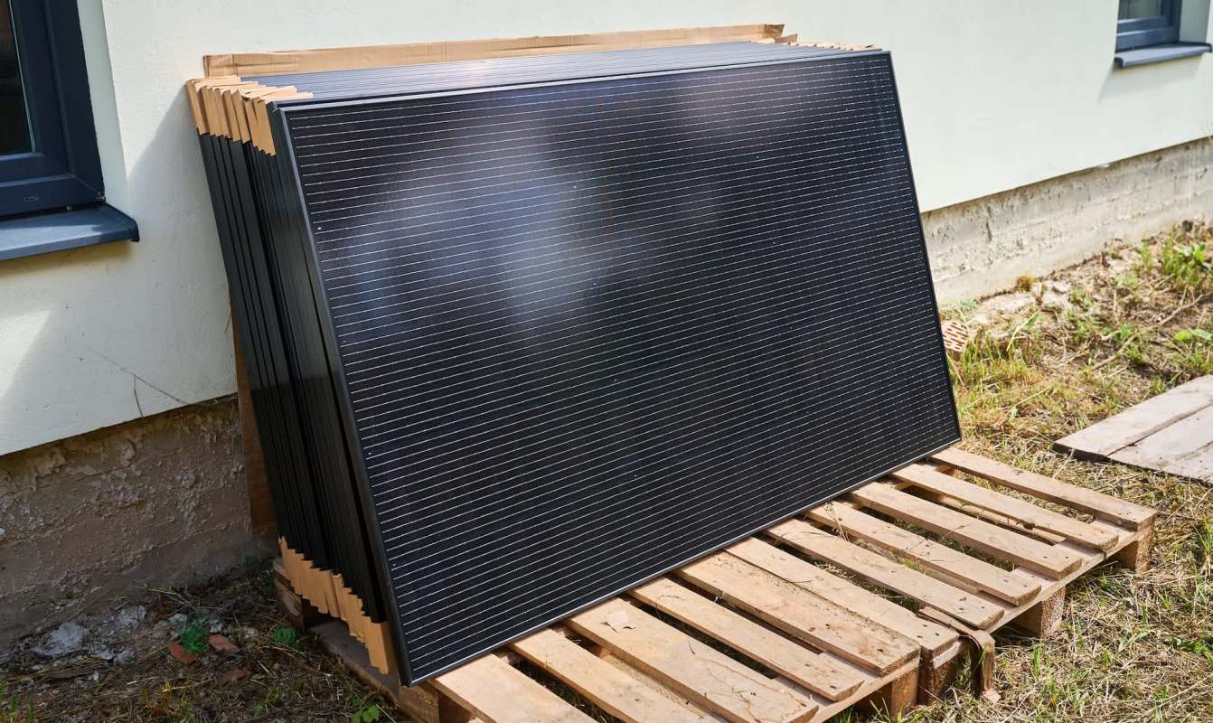 A stack of solar panels on a wooden pallet next to a building.