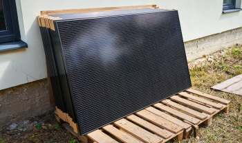 A stack of solar panels on a wooden pallet next to a building.