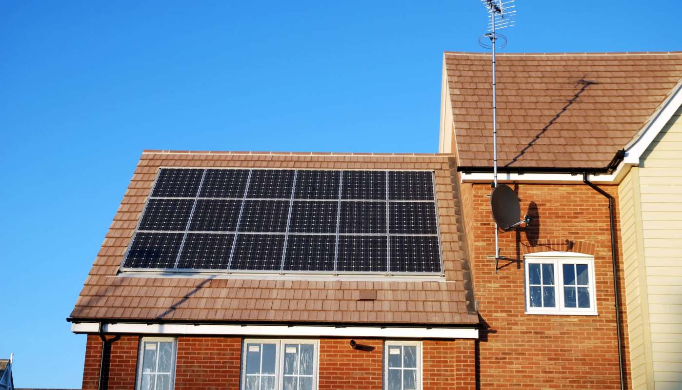 A house with rooftop solar panels under a clear blue sky.