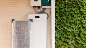 A solar panel and electrical equipment mounted on a wall beside green ivy.