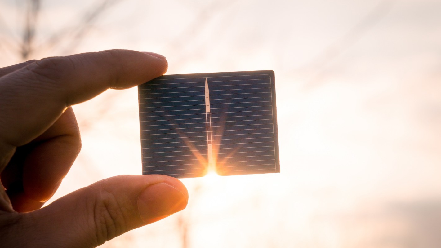 A hand holds a small solar panel against a bright background.