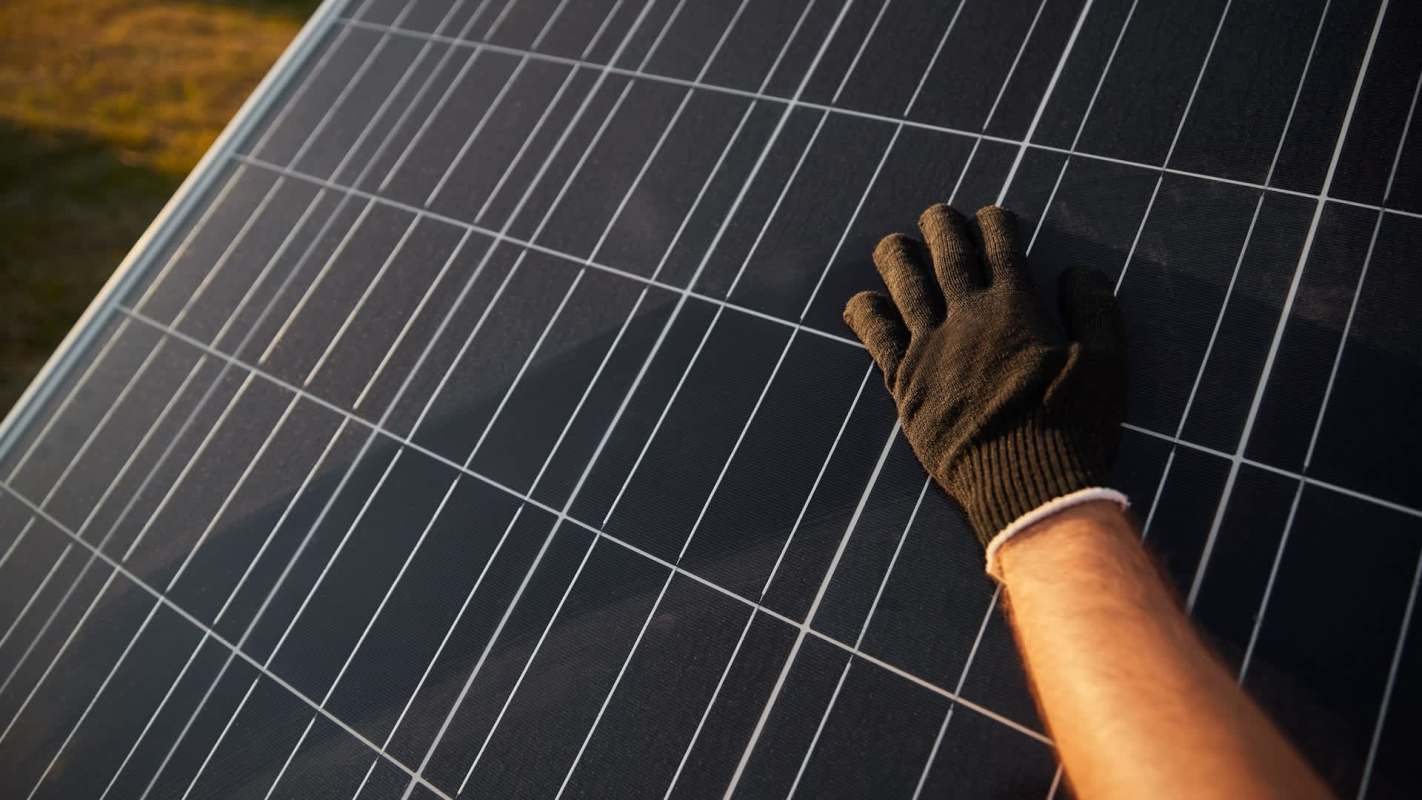 A hand in a black glove touches a solar panel.