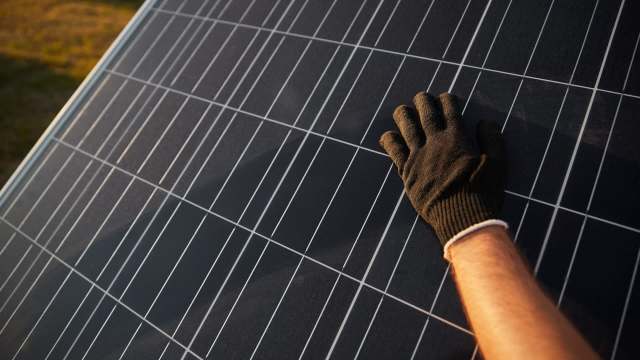 A hand in a black glove touches a solar panel.