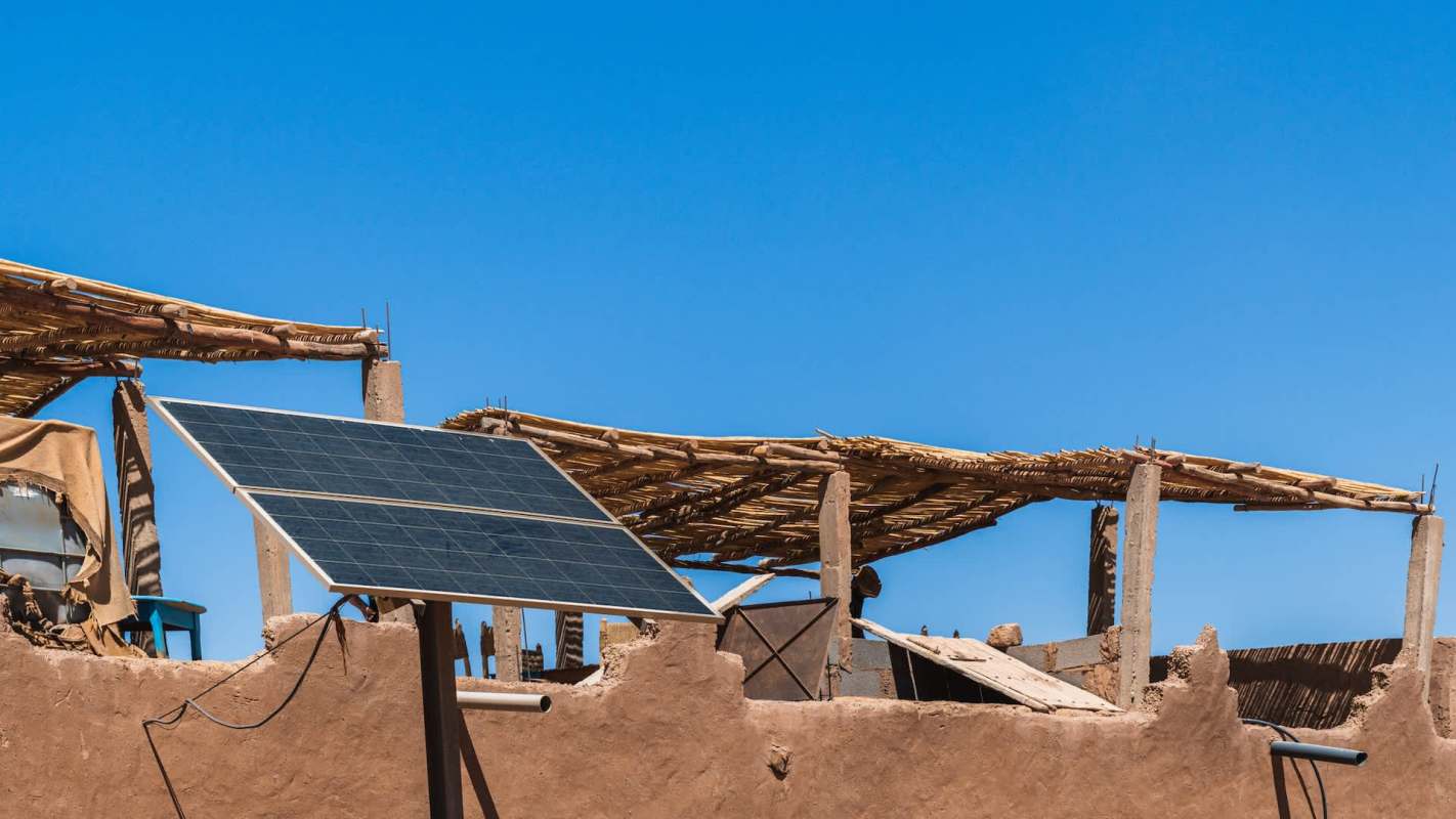 A mounted solar panel on a building with a thatched roof.