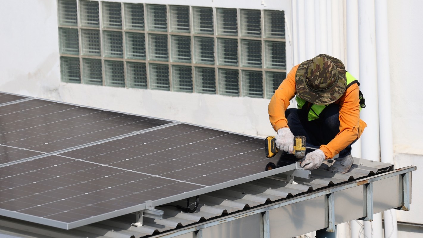 A worker installs solar panels on a rooftop.