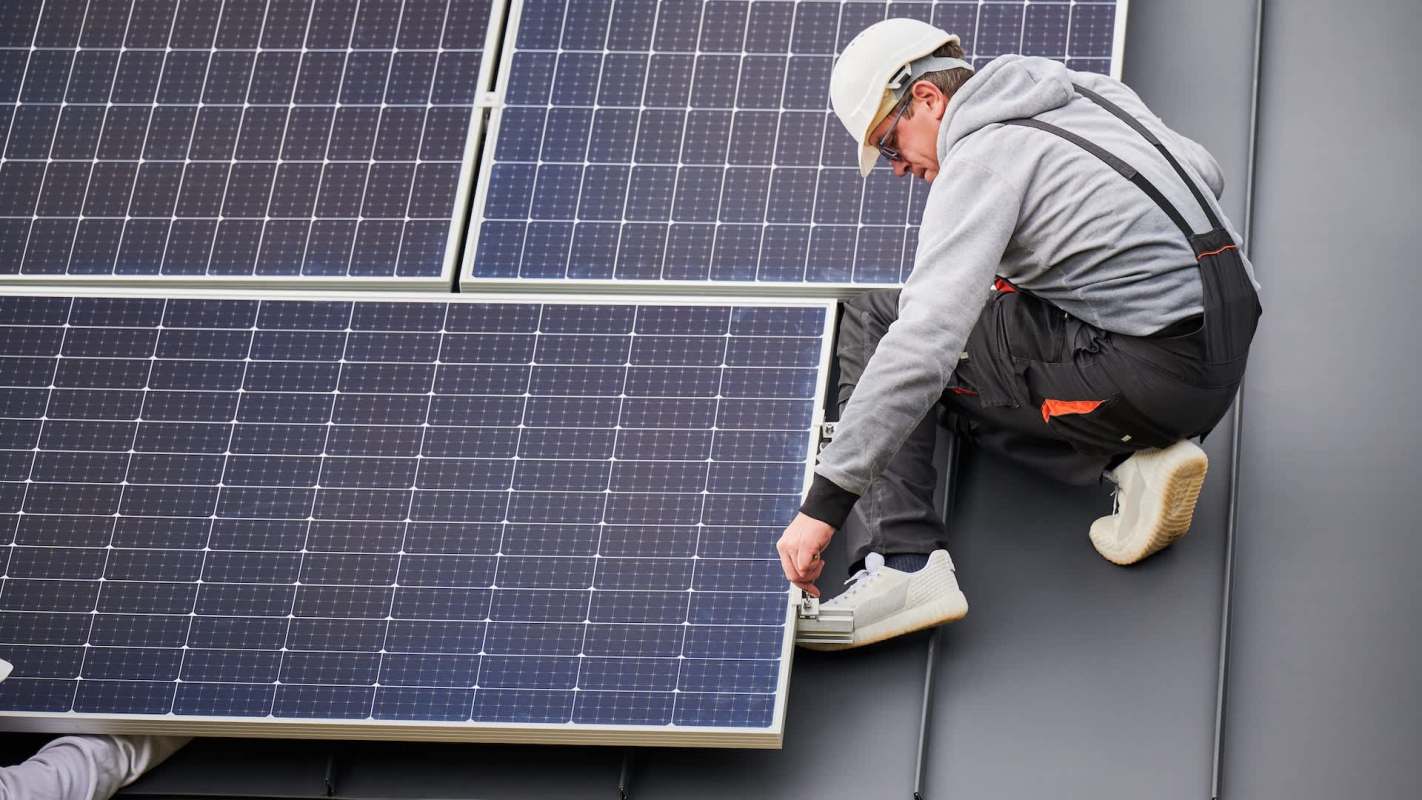 A worker installs a solar panel on a rooftop.