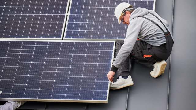 A worker installs a solar panel on a rooftop.
