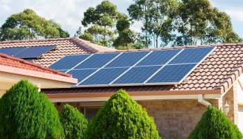 Solar panels installed on the roofs of two houses surrounded by hedges and trees.