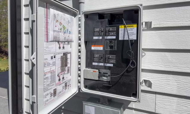 An open electrical panel with circuit breakers and a wiring diagram attached.