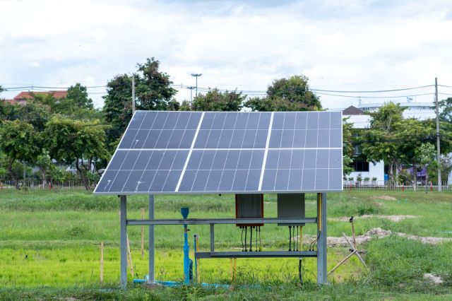 An angled solar panel stands in a grassy field