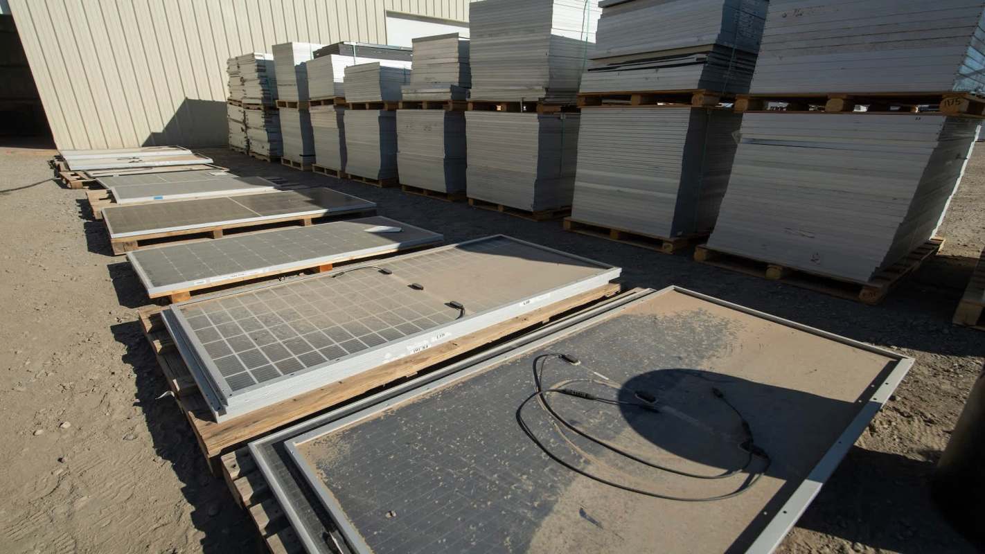 Solar panels and metal sheets stacked on pallets in a storage area.