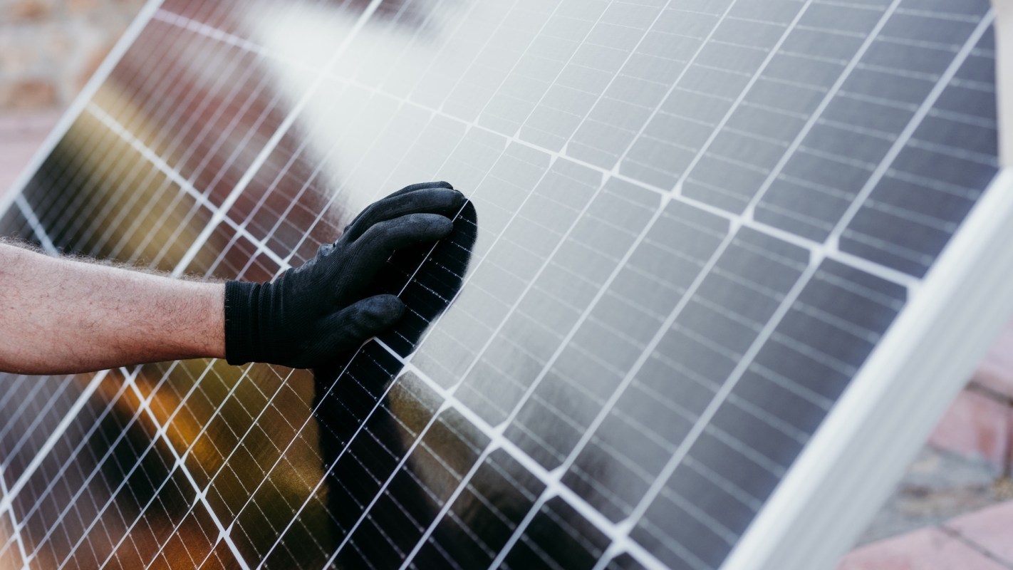 A hand wearing a black glove touches a solar panel.