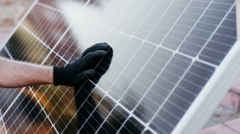 A hand wearing a black glove touches a solar panel.