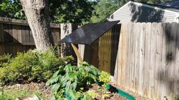 A solar panel installed on a wooden structure near a garden with plants and a wooden fence.