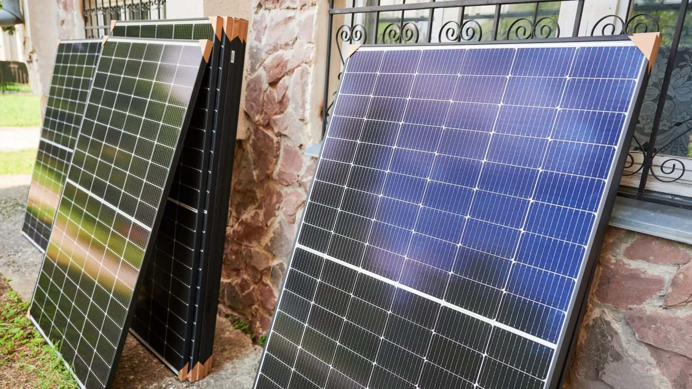 Several solar panels are propped against a stone wall near a window.