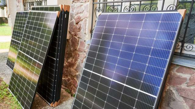 Several solar panels are propped against a stone wall near a window.