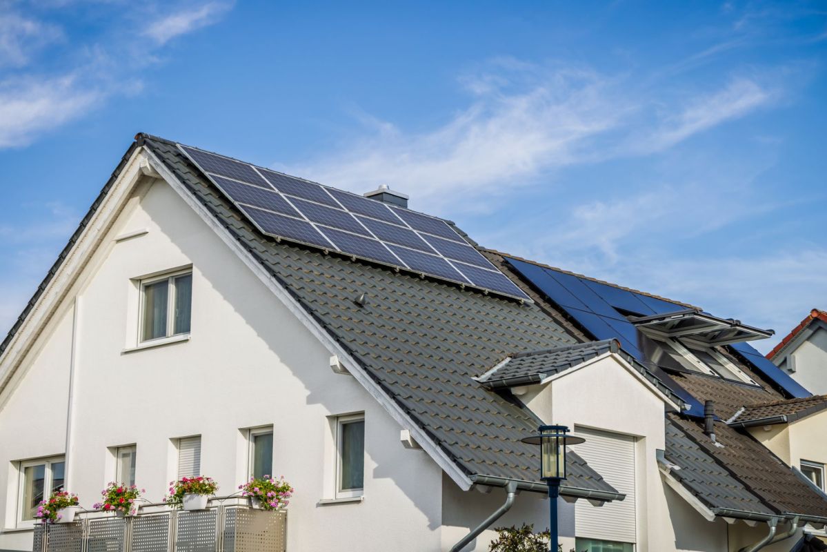 A house with solar panels on the roof and flower pots on the balcony.